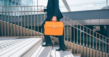 From the neck down view of a contemporary business walking upstairs in the city backlight, holding overnight bag - business, work concept